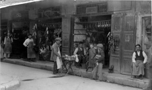 Σανδαλοποιεία στην οδό Αθηνάς, 1920 (Fred Boissonas):Η περιοχή της «Παλιάς Αγοράς», κοντά στο Μοναστηράκι, στο τέλος του 19ου αιώνα είχε πάψει να είναι το εμπορικό κέντρο της πόλης. Παρέμεινε, όμως, πιάτσα για μια σειρά από ειδικότητες, καθώς και εμπορικό κέντρο για φτηνά προϊόντα κατώτερης ποιότητας: στην ευρύτερη περιοχή, για παράδειγμα, βρισκόταν το λεγόμενο «Μπαγιατοπάζαρο», όπου οι φτωχοί της πόλης αγόραζαν μισοτιμής τρόφιμα που είχαν μπαγιατέψει. ©Πανεπιστημιακές Εκδόσεις Κρήτης.