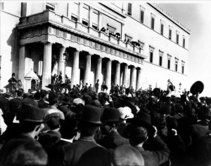 Ο βασιλιάς μιλάει στο πλήθος μετά το συλλαλητήριο της 14ης Σεπτεμβρίου 1909 (φωτογραφία Μιχ. Βελούδιου, ΕΛΙΑ):Το κίνημα στο Γουδί επιβλήθηκε οριστικά όταν φάνηκε ότι διαθέτει λαϊκή υποστήριξη, με την πραγματοποίηση μεγάλων διαδηλώσεων υπέρ του σε όλες τις πόλεις της χώρας. Κρίσιμος για την οργάνωση και την επιτυχία των διαδηλώσεων αυτών ήταν ο ρόλος του συνδέσμου συντεχνιών, της δευτεροβάθμιας οργάνωσης των επαγγελματικών σωματείων της εποχής. Στις «συντεχνίες» συμμετείχαν τόσο μισθωτοί όσο και μικροεργοδότες, ήταν όμως ξεκάθαρο ότι τον έλεγχό τους τον είχαν οι καταστηματάρχες. ©Πανεπιστημιακές Εκδόσεις Κρήτης.